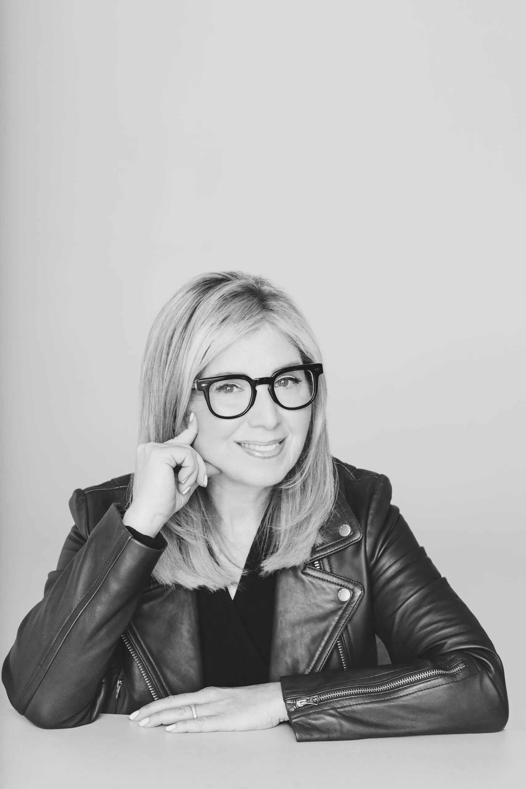 Leslie Zane in a leather jacket and glasses, resting her chin on her hand