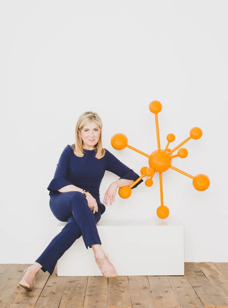 Leslie Zane seated beside an orange molecule sculpture